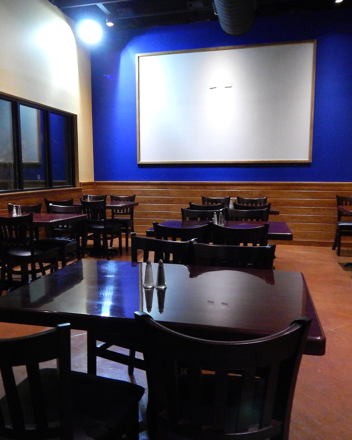 Casa Colombia's party room set with dark wood tables and chairs beneath a projector screen on a deep blue wall